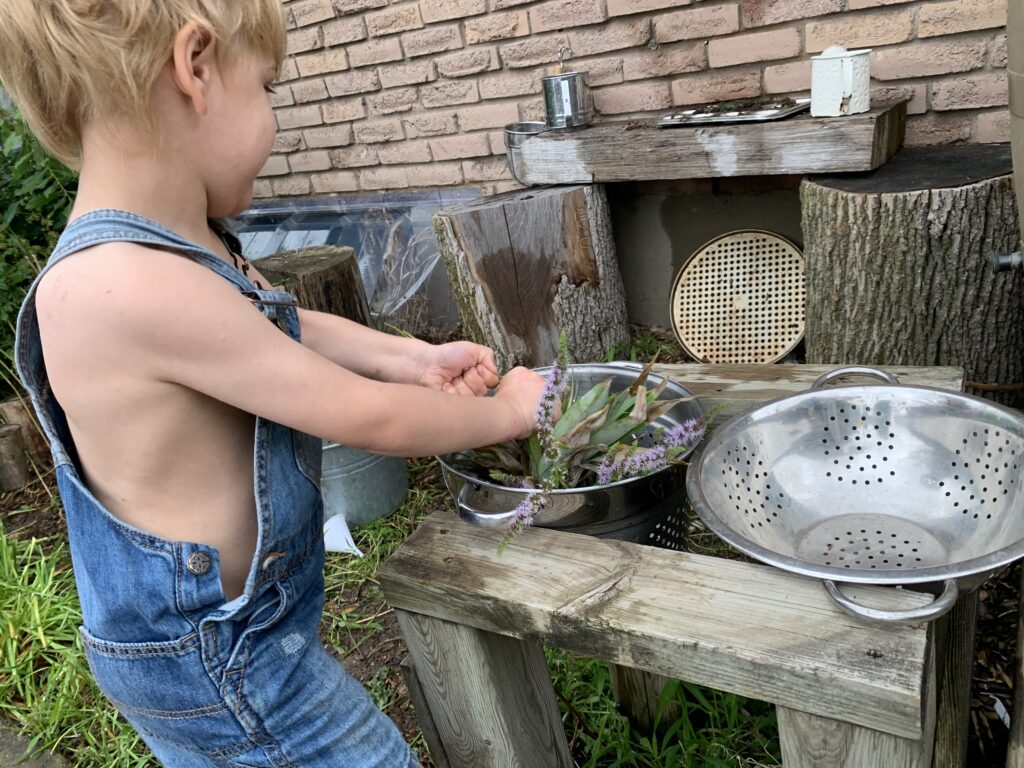 Child exploring mint sprigs and materials in our Montessori sensory garden